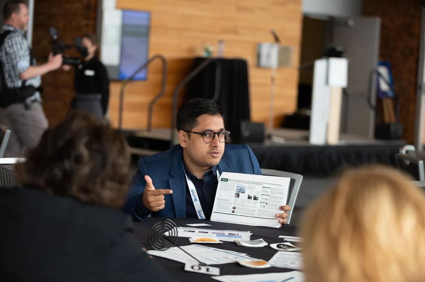 Three people sit at a table with scattered papers during the BlueTech Forum event in Vancouver, BC