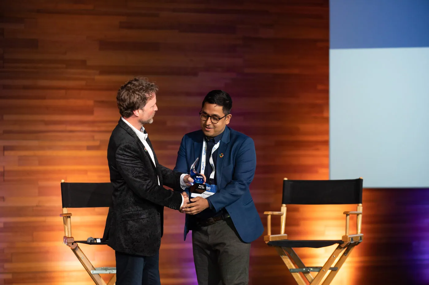 Two people stand on stage shaking hands and exchanging a BlueTech award