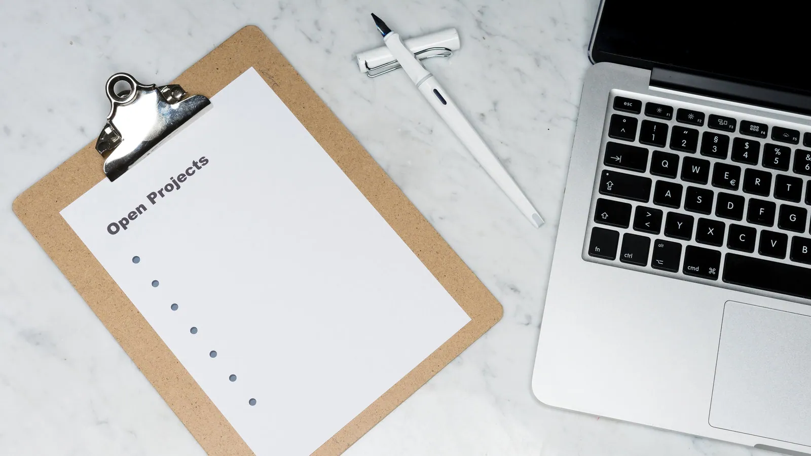 An image of a clipboard with the text "Open Projects" is next to a pen and silver laptop on a table.